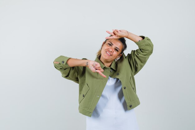 Young lady in t-shirt jacket showing v-sign and looking glad  