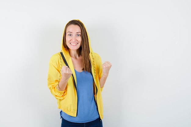 Young lady in t-shirt, jacket showing winner gesture and looking blissful