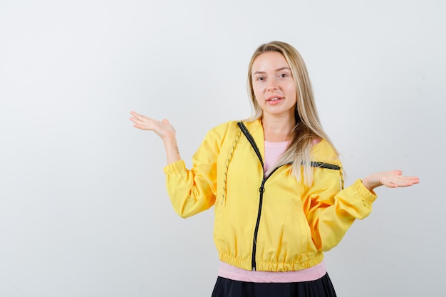 Young lady in t-shirt, jacket spreading palms aside and looking joyful