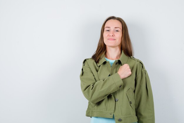 티셔츠를 입은 젊은 여성, 가슴에 주먹을 쥔 재킷, 자신감 있는 앞모습.