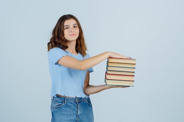 Free photo young lady in t-shirt, jeans holding books and looking satisfied , front view.