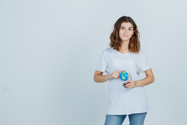 Young lady in t-shirt, jeans holding globe while standing and looking confident , front view.