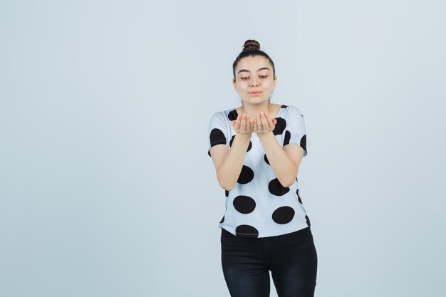 Free photo young lady in t-shirt, jeans sending kiss with hands and looking charming , front view.