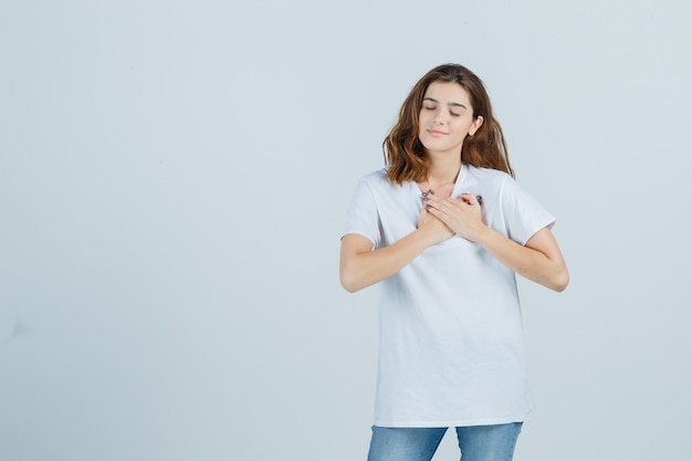 Молодая дама в футболке, джинсах показывает жест молитвы и выглядит обнадеживающим, вид спереди.