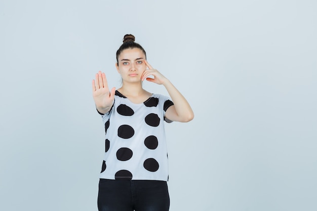 Giovane donna in t-shirt, jeans che mostrano il gesto di arresto e che sembrano seri, vista frontale.