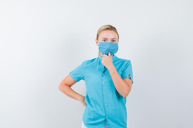 Young lady in t-shirt, mask holding hand on chin and looking confident