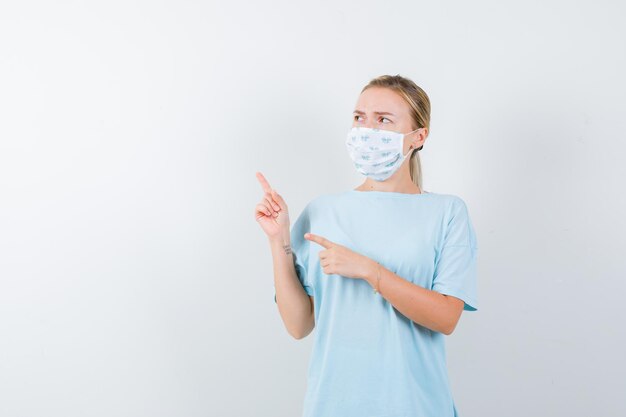 Young lady in t-shirt, mask pointing aside and looking serious