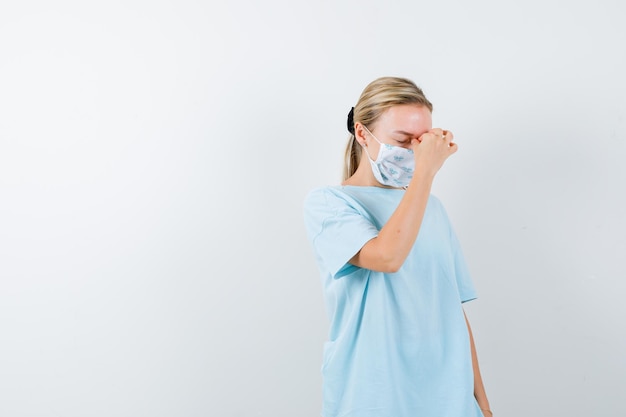 Young lady in t-shirt, mask rubbing nose and eyes and looking tired