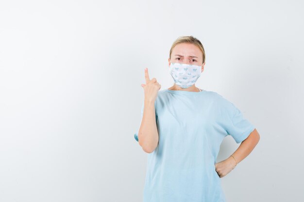 Young lady in t-shirt, mask showing a minute gesture and looking serious