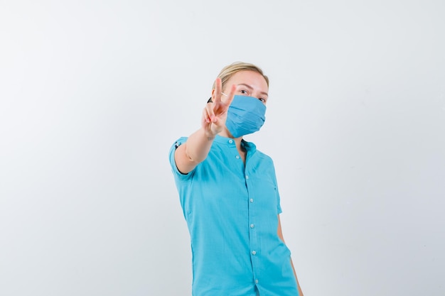 Young lady in t-shirt, mask showing victory sign and looking confident