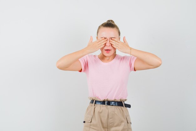 手で目を覆い、怖がって見えるTシャツとパンツの若い女性