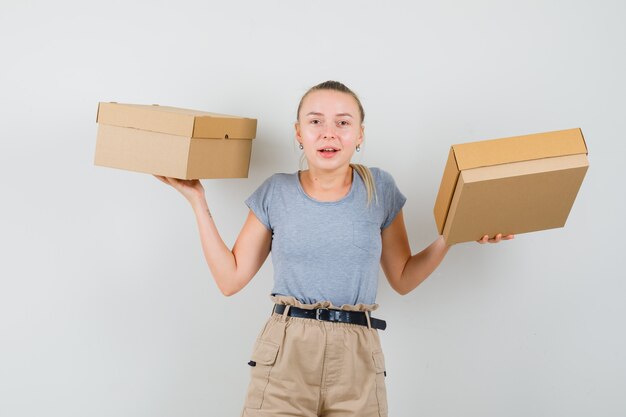 段ボール箱を保持し、幸せそうに見えるTシャツとズボンの若い女性