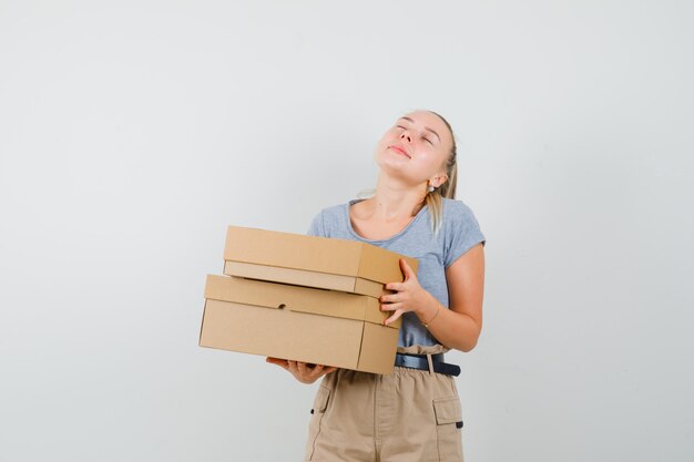 Молодая дама в футболке и штанах держит картонные коробки и выглядит мирно