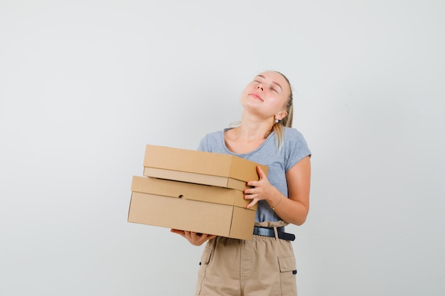 Young lady in t-shirt and pants holding cardboard boxes and looking peaceful