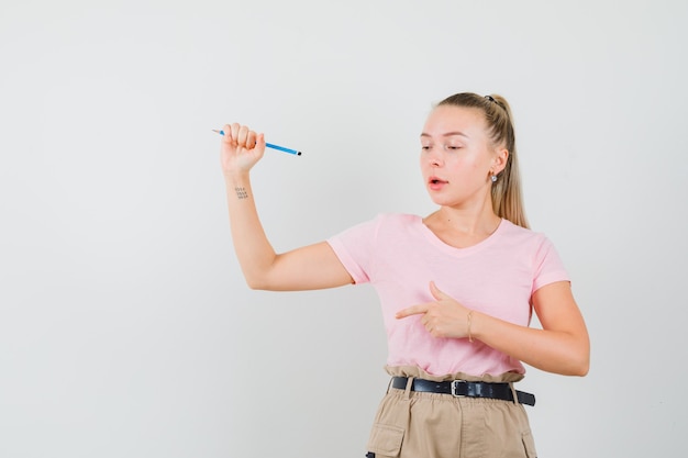 Young lady in t-shirt and pants holding pencil, pointing down and looking focused