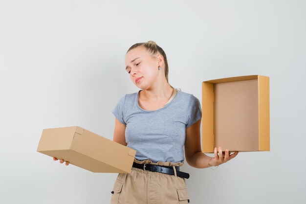 Young lady in t-shirt and pants looking into cardboard box and looking disappointed