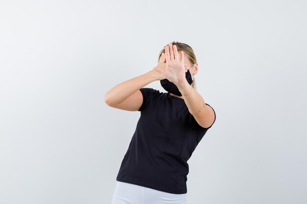 Young lady in t-shirt, pants, medical mask holding hand isolated