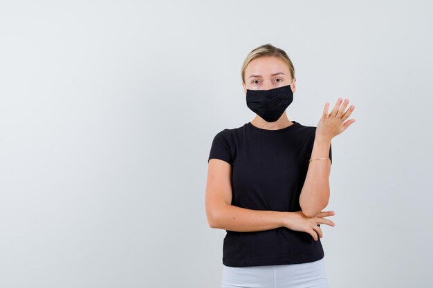 Young lady in t-shirt, pants, medical mask stretching hand isolated