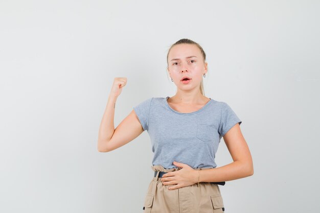 親指で後ろを向いて疑わしいTシャツとズボンの若い女性