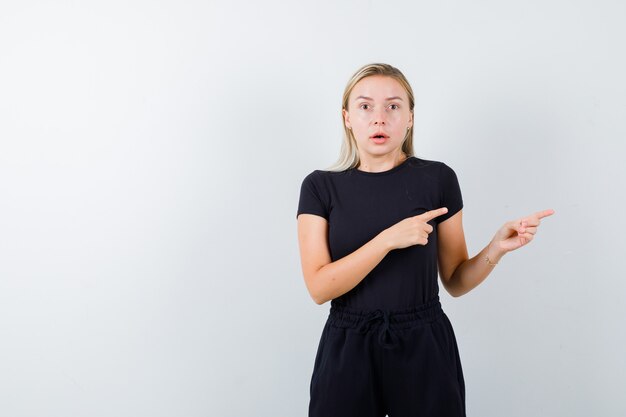 Young lady in t-shirt, pants pointing to the right side and looking indecisive , front view.