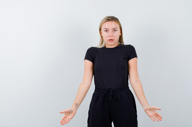 Young lady in t-shirt, pants showing palms and looking careful , front view.