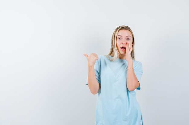 Young lady in t-shirt pointing to the left side with thumb isolated