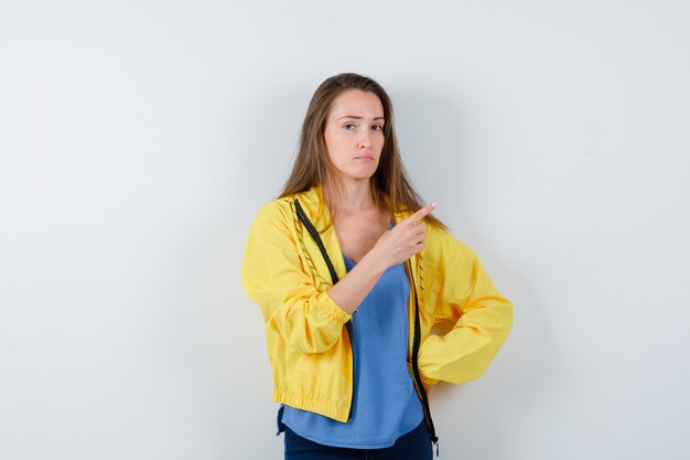 Young lady in t-shirt pointing at upper right corner and looking sensible , front view.