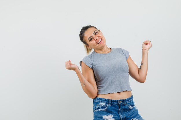 Young lady in t-shirt, shorts showing winner gesture and looking glad