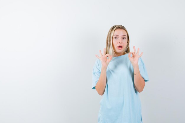 Young lady in t-shirt showing ok gesture and looking puzzled isolated