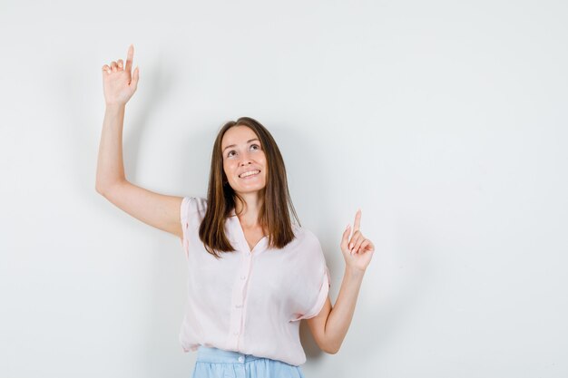 Young lady in t-shirt, skirt pointing up and looking focused , front view.