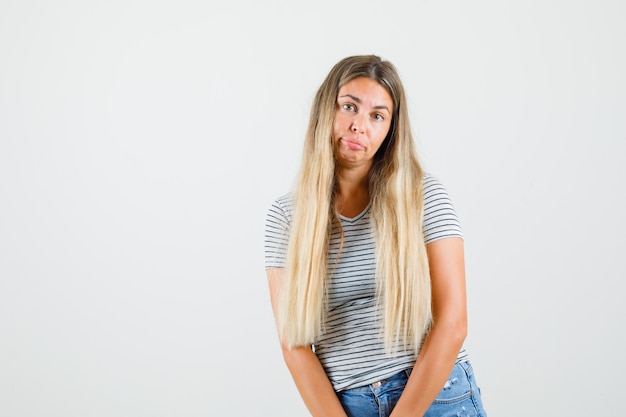 Young lady in t-shirt standing and looking upset , front view.