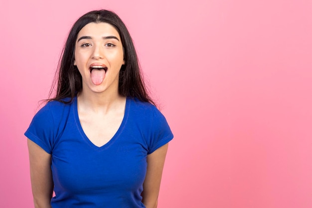 Young lady taking out her tongue and standing on pink background