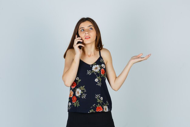 Young lady talking on mobile phone in blouse, skirt and looking clueless , front view.