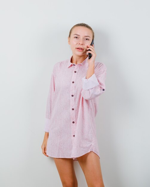 Young lady talking on mobile phone in pink shirt and looking optimistic