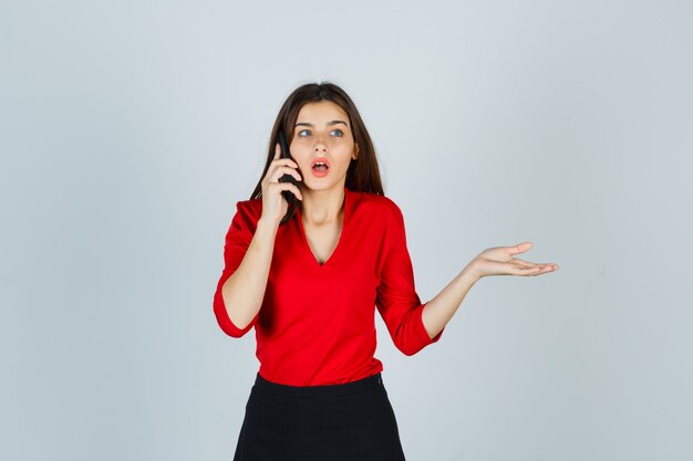 Young lady talking on mobile phone in red blouse, skirt and looking puzzled