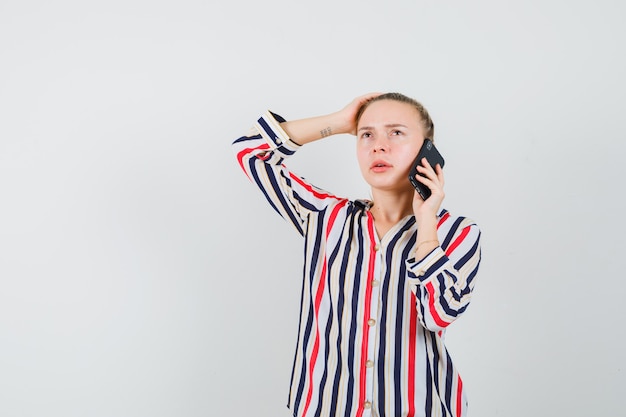 Young lady talking on mobile phone in striped shirt and looking pensive