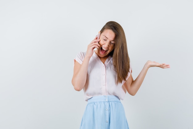 Young lady talking on mobile phone in t-shirt, skirt and looking glad. front view.