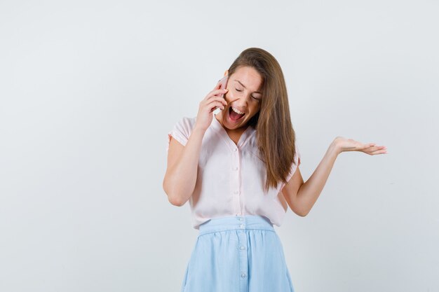 Tシャツ、スカート、嬉しそうに携帯電話で話している若い女性。正面図。