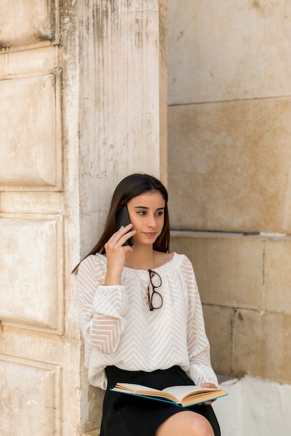 Foto gratuita giovane donna che comunica sul telefono mentre si tiene il libro