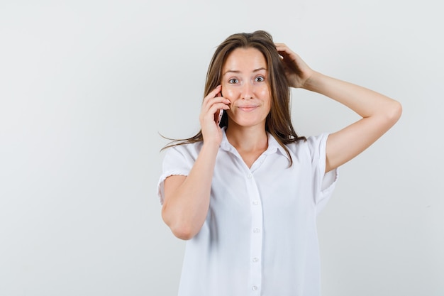 Young lady talking on phone in white blouse and looking puzzled.