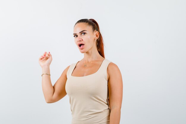 Young lady in tank top pointing back and looking astonished , front view.