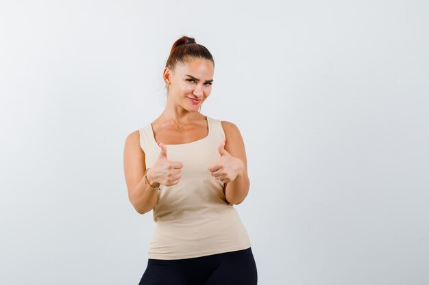 Young lady in tank top showing double thumbs up and looking happy , front view.