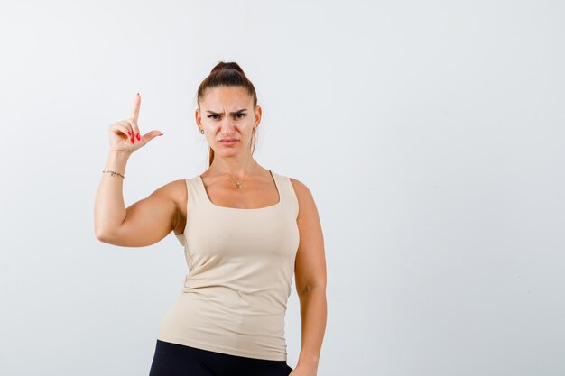 Young lady in tank top showing gun gesture and looking serious , front view.