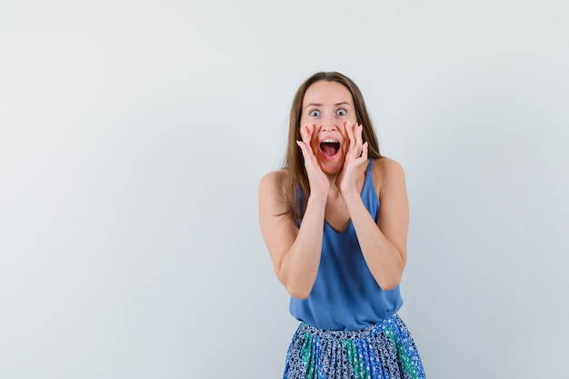 Young lady telling secret or shouting in singlet, skirt and looking excited , front view.