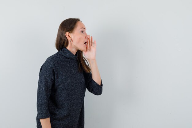 シャツの口の近くで手で秘密を語る若い女性