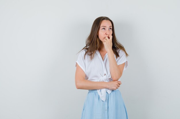 Young lady thinking something in blouse, skirt and looking pensive