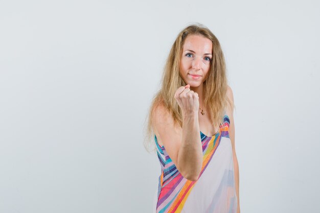 Young lady threatening with clenched fist in summer dress and looking confident 