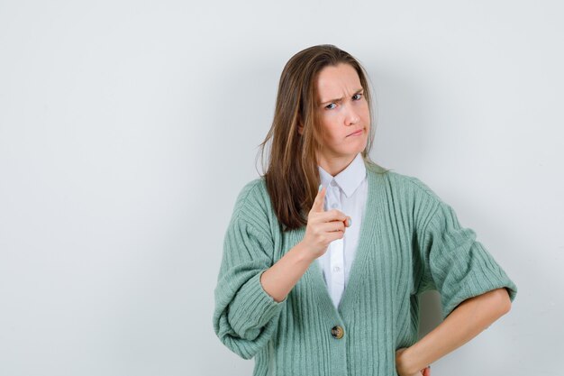 Young lady threating with finger in shirt, cardigan and looking serious. front view.