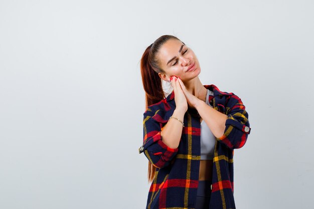 Young lady in top, plaid shirt leaning on hands as pillow and looking sleepy , front view.