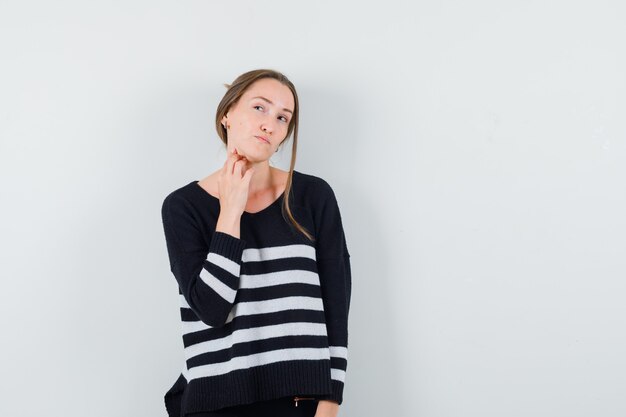 Young lady touching her neck in casual shirt and looking hesitant